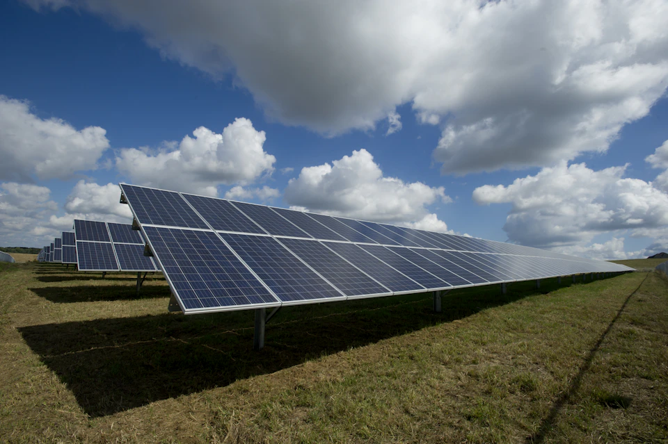 Hileras de paneles solares fotovoltaicos en un campo verde bajo un cielo azul con nubes