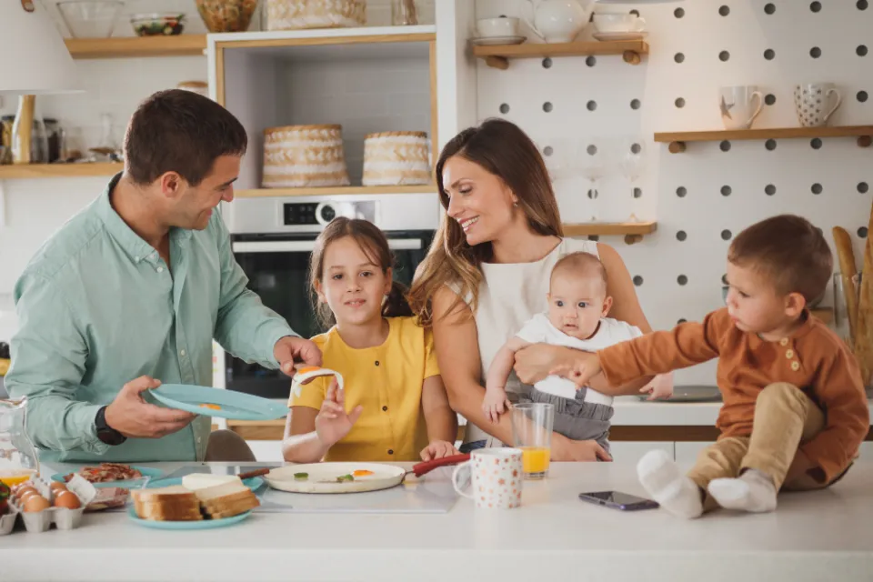 Familia con niños pequeños desayunando y riendo en la cocina de casa