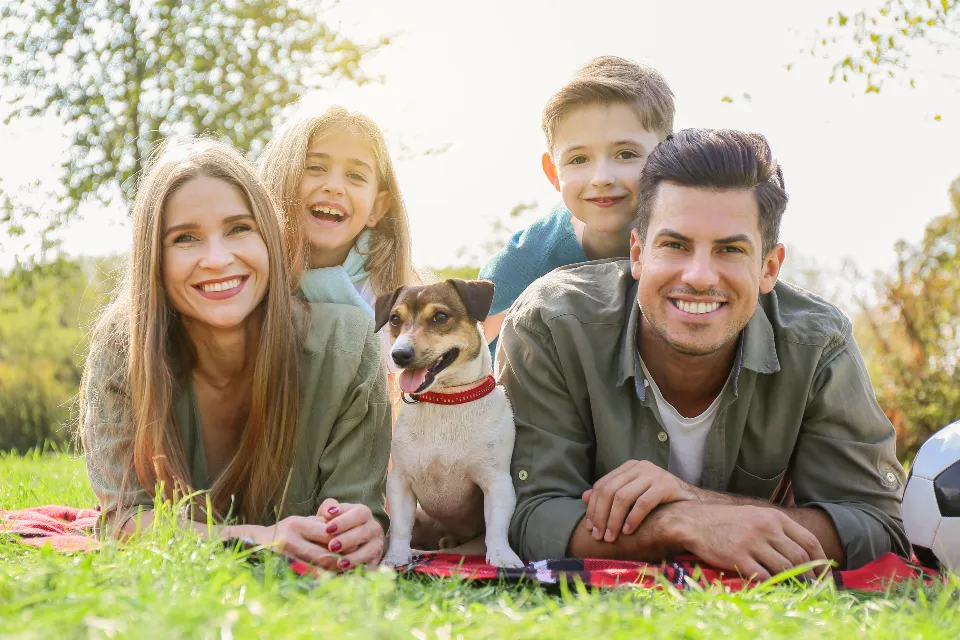 Familia sonriendo en el campo con su perro, sentados en una manta