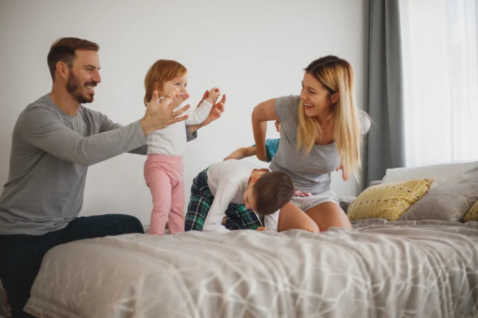 Padres jugando con sus hijos en la cama, riendo en casa